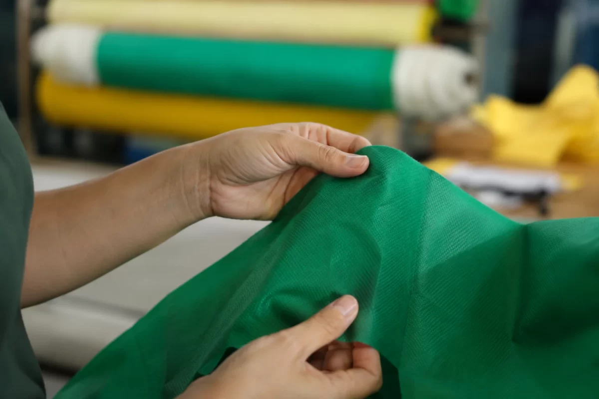 Mãos avaliando a textura de um tecido TNT verde na confecção