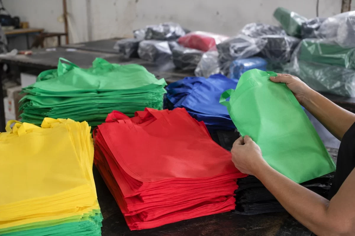 Pilhas de sacolas de TNT em cores variadas na bancada de produção