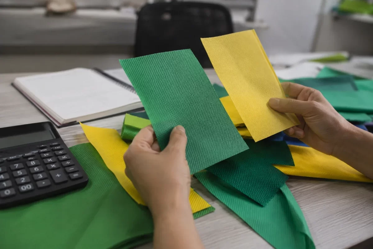 Comparando amostras de TNT verde e amarelo com calculadora na mesa de orçamento